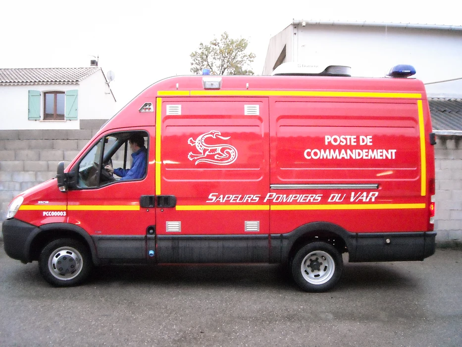 Gros plan détaillé d'une camionnette utilitaire blanche stationnée, montrant le flanc du véhicule avec un marquage professionnel de signalétique (lettres peintes, logos, design graphique coloré) clairement visible et net, photographié sous lumière naturelle en extérieur urbain ou commercial, mettant en avant la qualité et la précision du travail de marquage réalisé.
